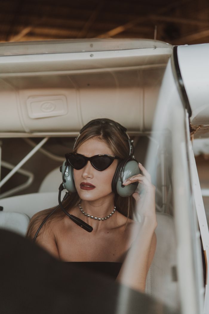 Services Stylish woman wearing sunglasses and headset in airplane cockpit.