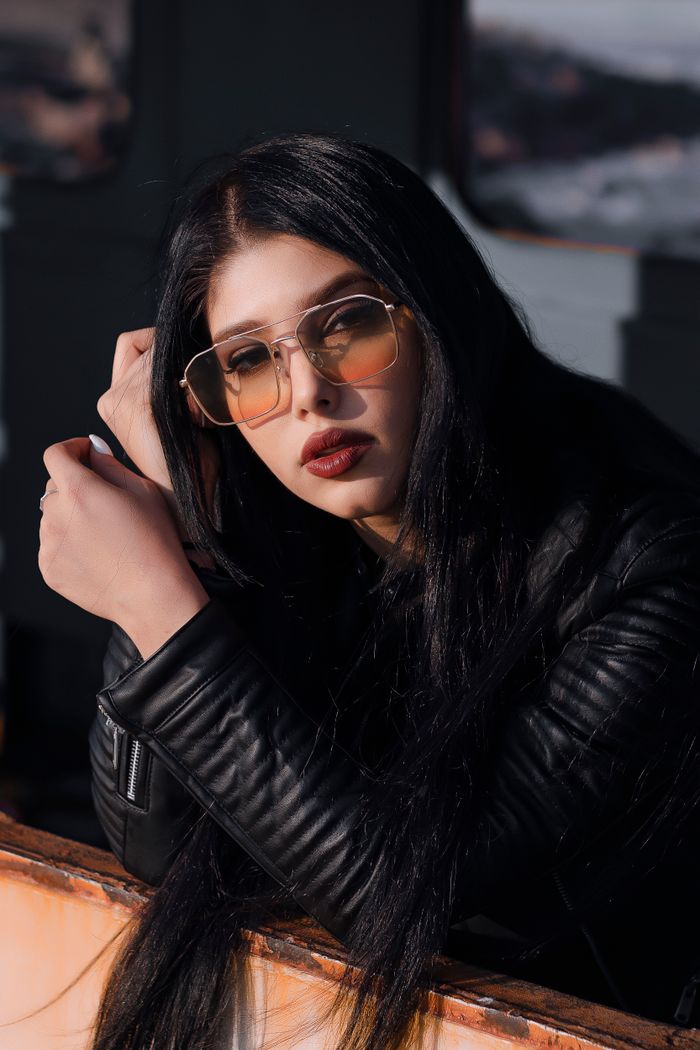 About Fashionable woman posing confidently in a black leather jacket and sunglasses.