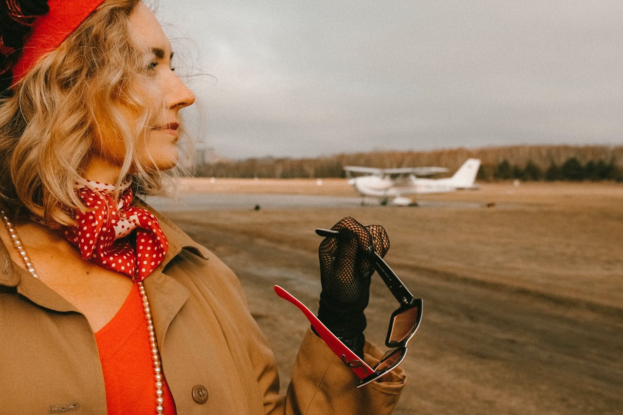 Services A fashionable woman with a red scarf and sunglasses standing near a small airplane.