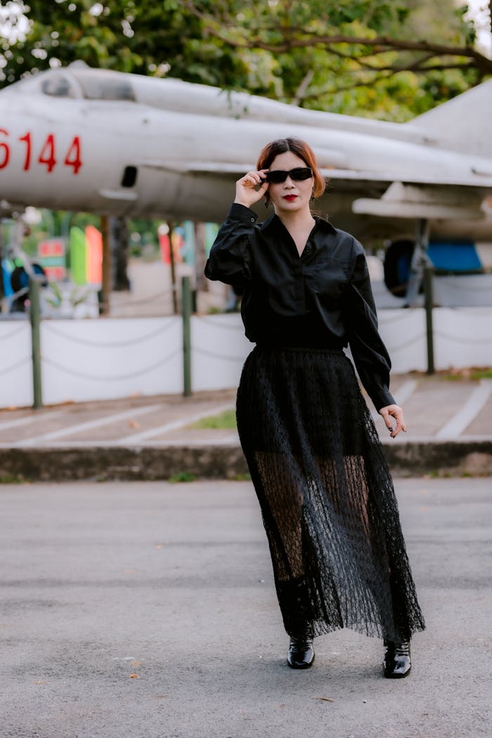 About Stylish woman in black outfit posing confidently by a vintage aircraft.
